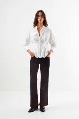 Camisa blanca de algodón con cuello mao, manga larga y diseño estructurado con pinzas que ajustan la cintura. Presenta bolsillos de parche en el pecho y un escote en V profundo sin botones visibles en la parte superior.
