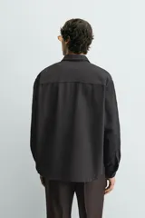 Sobrecamisa de corte relajado confeccionada en denim de algodón con diseño a rayas verticales. Presenta cuello solapa, cierre frontal de botones, manga larga con puños abotonados y un bolsillo plastrón en el pecho.