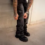 Pantalón de jean negro de corte flared con efecto desgastado, tiro medio y detalles de pedrería y tachas formando patrones en los laterales de las piernas.
