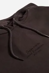 Buzo canguro Mistral modelo Alex de felpa sin frisa, color marrón oscuro. Cuenta con capucha ajustable con cordón, bolsillo frontal tipo canguro, puños y ruedo elásticos, y lettering estampado en el pecho.
