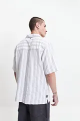 Camisa de manga corta a rayas verticales blancas y grises, con cuello camisero y corte recto. El modelo usa talle M.