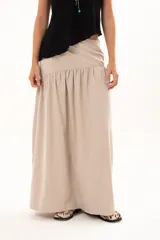 Pollera larga de corte evasé en color arena, con detalle de costura horizontal y frunces en la parte inferior que le otorgan volumen y movimiento.