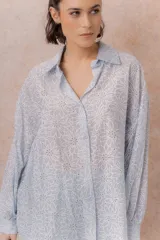 Camisa lila oversize de algodón con bordado floral calado tipo broderie, cuello camisero, manga larga y abotonadura frontal.
