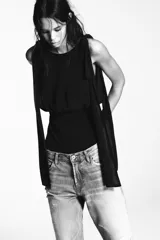 Body negro de cuello barco y tirantes con aplicación de lazos a tono. Cierre en bajo con botones a presión y en espalda con cremallera.