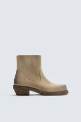 Bota cowboy de caña media, color beige claro con efecto desgastado. Fabricada en piel serraje engrasado, presenta horma cuadrada y tacón ancho de madera a contraste.