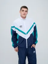 Campera deportiva Umbro modelo Beat, confeccionada en nylon ligero con diseño de bloques de color en blanco, azul marino y verde azulado. Presenta cierre frontal, cuello alto y elásticos en puños y cintura.