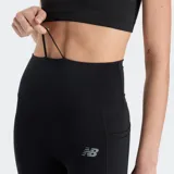 Calza deportiva New Balance de tiro alto, color negro, con tecnología NB DRY para absorción de sudor. Presenta bolsillos laterales y logo de la marca en la pierna.