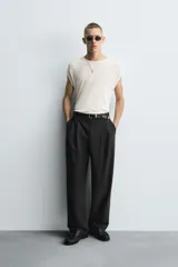 Pantalón negro de corte ancho con pliegues frontales dobles, bolsillos delanteros y traseros de vivo. Cierre frontal con cremallera y botón.