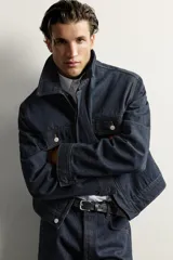 Campera de denim azul oscuro de corte cropped, con cuello camisero, bolsillos delanteros con solapa y cierre frontal oculto con botones metálicos.