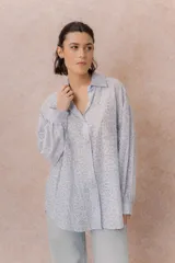 Camisa lila oversize de algodón con bordado floral calado tipo broderie, cuello camisero, manga larga y abotonadura frontal.