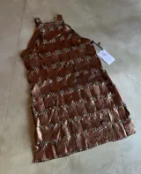 Vestido corto de tirantes, color cobre metalizado, con construcción tejida a base de tiras de material sintético unidas por argollas metálicas plateadas.