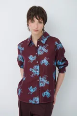 Camisa de corte clásico con cuello camisero y cierre frontal de botones, confeccionada en tela color bordó con estampado floral en tonos celestes.