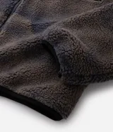 Campera de sherpa con estampado camuflado en tonos marrones y grises, de corte oversize y manga larga. Presenta cuello alto, cierre frontal completo y un bolsillo frontal contrastante en color negro con cierre.
