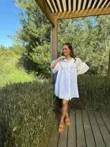 Vestido camisero blanco de lino italiano, con cuello camisero, cierre frontal con botones, mangas cortas con doble volado y bolsillos laterales.