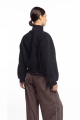 Campera negra de cuello alto con cierre frontal metálico completo, bolsillos laterales y logo bordado en el pecho.