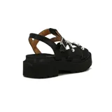 Sandalia Vizzano para mujer, color negro, de suela track y taco bajo. Presenta tiras cruzadas en el empeine decoradas con tachas metálicas plateadas semiesféricas y una tira ajustable con hebilla en el tobillo.