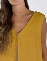 Vestido largo sin mangas de lino, con escote en V y diseño bicolor que combina un tono beige en el frente y un panel lateral en color fucsia. Presenta una costura central visible con detalle desflecado y un ruedo con volado.