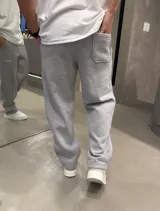 Pantalón de jogging baggy color gris melange, con cintura elástica, bolsillos laterales, costuras frontales en relieve y pequeño estampado con texto en la pierna izquierda.