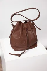 Cartera tipo botellero color marrón con efecto trenzado, tamaño mediano, cierre con frunce, correa ajustable con hebilla para usar al hombro o cruzada, doble bolsillo interior (uno con cierre).