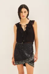 Falda corta de tiro medio con diseño cruzado, confeccionada en viscosa crepe. Presenta un acabado íntegramente bordado con lentejuelas y piedras decorativas en el ruedo. Incluye cierre posterior y forrería a tono.