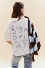 Remera blanca de manga corta con estampado lineal en color azul que incluye ilustraciones de elementos típicos como un mate, un termo, un pájaro, el sol y olas.
