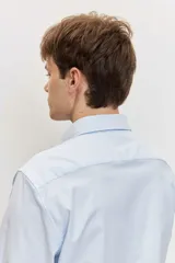 Camisa de manga larga con cierre frontal de botones y cuello clásico, color celeste con sutiles rayas verticales.