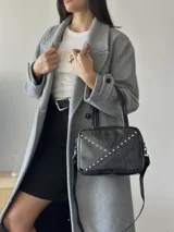 Cartera rígida negra de cuero con tachas plateadas y tres combinaciones de cuero diferentes que aportan textura. Tiene herrajes y cierre metálico plateado marca YKK. Cuenta con un asa fina para llevar al hombro o en la mano y una correa larga extra regulable.