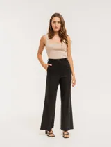 Pantalón negro de lino, tiro alto, corte palazo, con elástico en la pretina trasera, cierre delantero y broche interno. Tiene bolsillos laterales, dobladillo invisible y tajos a los costados.