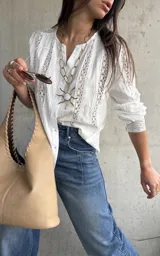 Camisa blanca de manga larga con detalles de encaje y diseño abotonado en la parte delantera.
