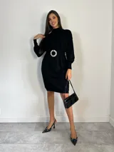 Vestido tipo polerón de tejido de punto color borgoña, con cuello alto, mangas largas con puños ajustados y corte recto. Incluye un cinturón del mismo material con una hebilla decorativa de flor con cristales.