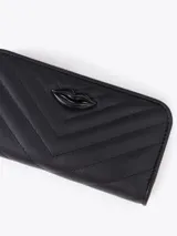 Maxi billetera de cuero vacuno con diseño matelassé en forma de V. Presenta un aplique metálico dorado en forma de labios en el frente y cierre perimetral con tirador de cuero.