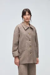 Chaquetón de lana fina sin teñir, con cuello camisero, cierre frontal de botones y bolsillos delanteros. Diseño de corte recto y estructura clásica.