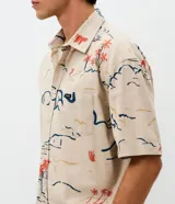 Camisa de corte relajado con cuello solapa y manga corta, confeccionada en algodón con estampa abstracta de palmeras y paisajes en tonos tierra, azul y rojo.