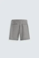 Bermuda negra de corte recto, con cintura elástica ajustable mediante cordón, pliegues frontales y bolsillos de vivo en la espalda. El bajo tiene un dobladillo vuelto.