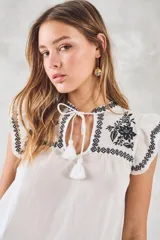 Blusa de color blanco con detalles bordados en negro, cuello redondo con cordones ajustables y mangas cortas con volados.