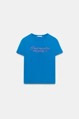 Camiseta de corte slim fit en color azul, con cuello redondo y manga corta. Presenta un detalle de texto estampado con aplicación de brillos en contraste en la parte frontal.