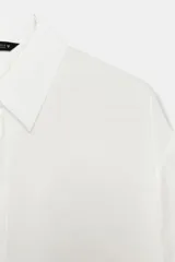 Camisa de corte fluido con cuello solapa y manga corta con dobladillo. Presenta cierre frontal con botones ocultos bajo una tapeta.