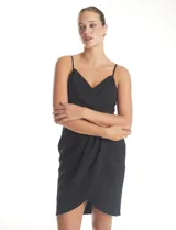 Vestido corto de crepe color negro con escote en V cruzado y drapeado en el busto. Presenta una falda envolvente con diseño drapeado y abertura asimétrica en el bajo, con cierre invisible en la espalda y forro interno.