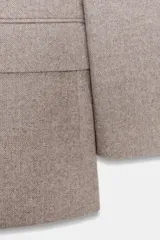 Blazer de corte sastrero confeccionado en tejido de lana con diseño de espiga. Presenta cuello con solapas, hombreras, cierre frontal con un botón y bolsillos delanteros con solapa.