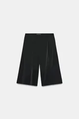 Bermuda de tiro medio color negro con pliegues delanteros y bolsillos laterales ocultos en costura. Cuenta con cierre delantero con cremallera, botón y ganchos metálicos.