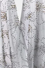 Top halter de tul color gris claro, con escote fluido drapeado y espalda descubierta. Presenta bordados con aplicación de abalorios en tonos oscuros y dorados.