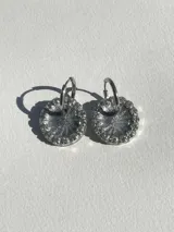 Aros colgantes con forma circular, hechos de resina color lila y borde de strass plateado. El aro es de acero quirúrgico plateado.