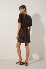 Vestido corto con escote en V y mangas cortas amplias, con elástico fruncido en la cintura. Presenta un teñido tie-dye en tonos marrón oscuro y verde azulado, con un borde de bordado de hilos de lurex plateado en el escote.