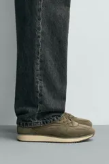 Zapatilla deportiva de estilo casual, confeccionada en una combinación de piezas de cuero con acabado de gamuza y paneles textiles. Presenta una horma redonda, cierre mediante cordones y una suela dentada en tono contrastante.