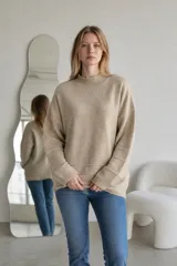 Sweater de punto color crema, con cuello alto y diseño holgado. Presenta puños y ruedo acanalados con detalle de líneas horizontales en la parte inferior.