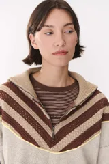 Buzo de tejido de punto con diseño combinado en colores beige y marrón. Presenta cuello alto con cierre frontal parcial, corte oversized y largo a la cadera. El diseño incluye detalles de textura en el tejido y una línea de color amarillo en la unión de los paneles.
