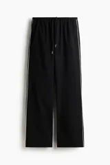 Pantalón negro de corte holgado y perneras rectas, con cintura elástica revestida y cordón ajustable. Cuenta con una línea blanca decorativa a lo largo de los laterales externos.