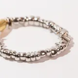 Pulsera elástica con cuentas irregulares plateadas y una cuenta central ovalada dorada.