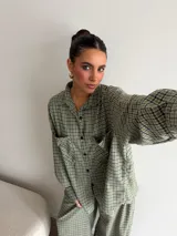 Camisa de corte oversize confeccionada en viyela con estampado de cuadros en tonos verdes y negros. Presenta cuello clásico, cierre frontal con botones oscuros y dos bolsillos delanteros amplios.