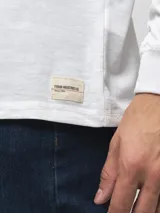 Remera de manga larga con cuello redondo, confeccionada en algodón, de corte clásico y diseño minimalista con detalle de etiqueta pequeña en el ruedo.